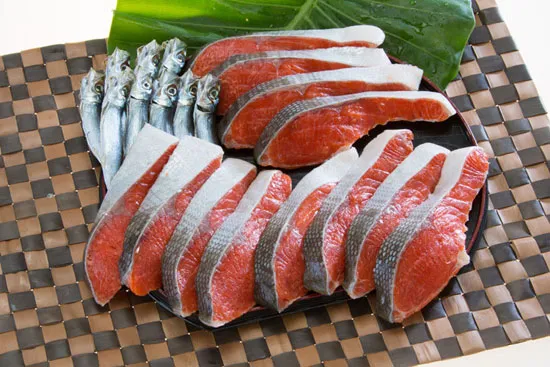 光洋の塩紅さけ 3味セットの商品写真。おいしそうな鮭の切り身が１２枚、うるめ鰯の干物が１０尾、お盆の上に並んでいる写真。